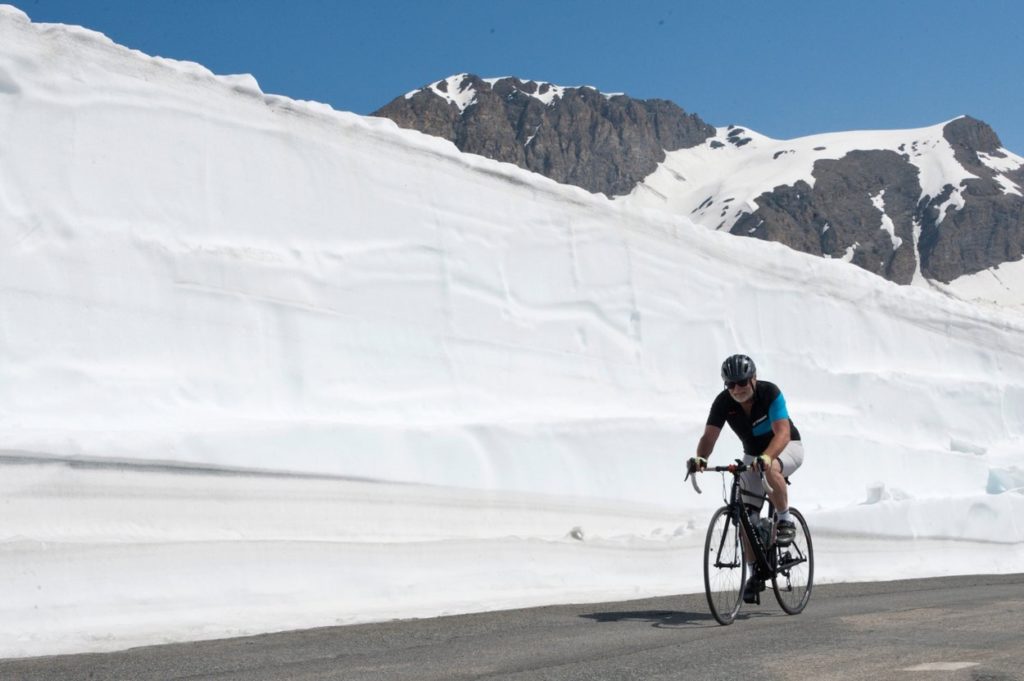 Val d'Isere, Savoie, France. 20th June 2018. People drive and ride past huge walls of snow on the road over The Col de l'Iseran - the highest pass in Europe at 2,764 metres above sea-level - after a winter season of reportedly the largest quantities of s